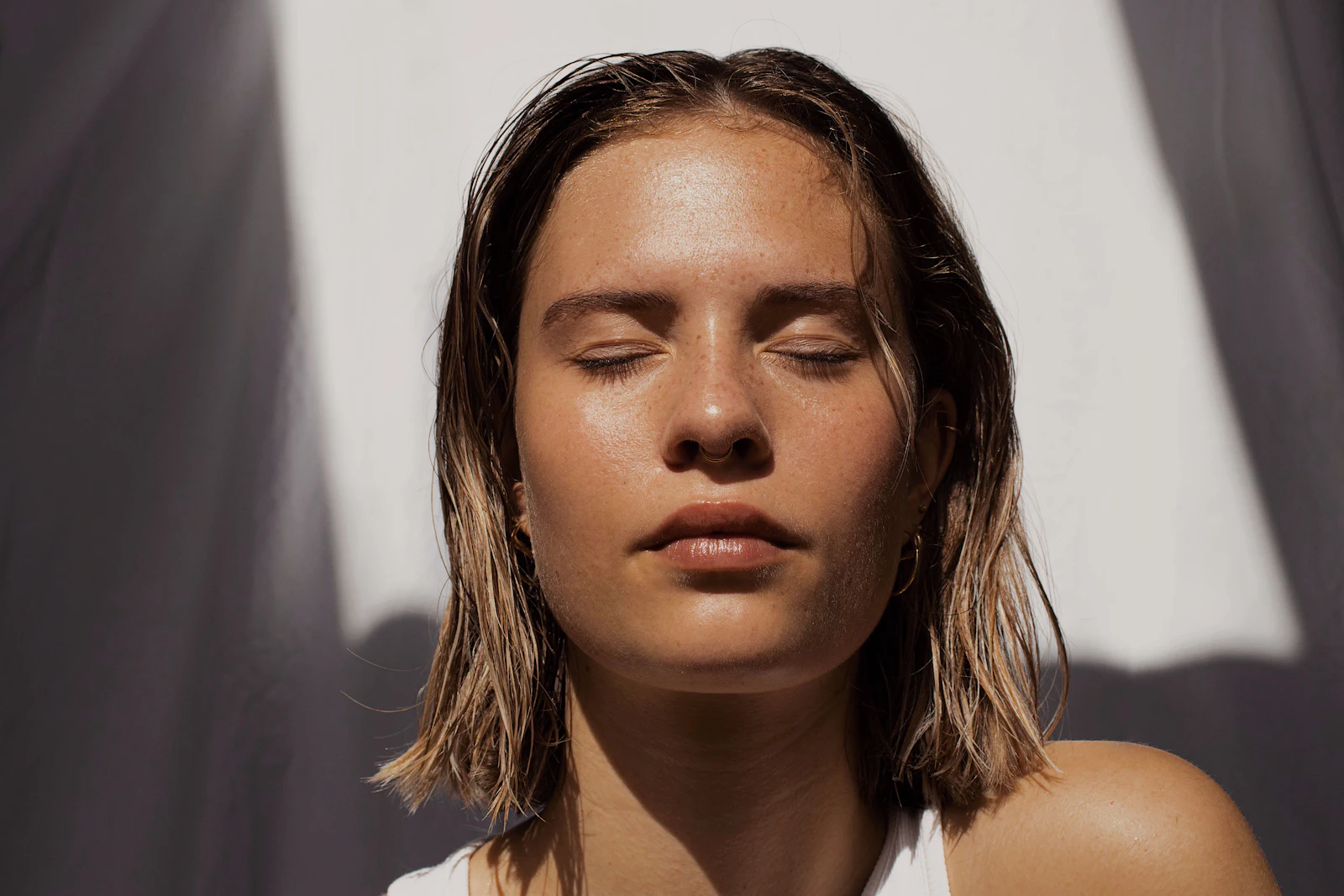 Mulher de olhos fechados e pele luminosa, sob luz natural
